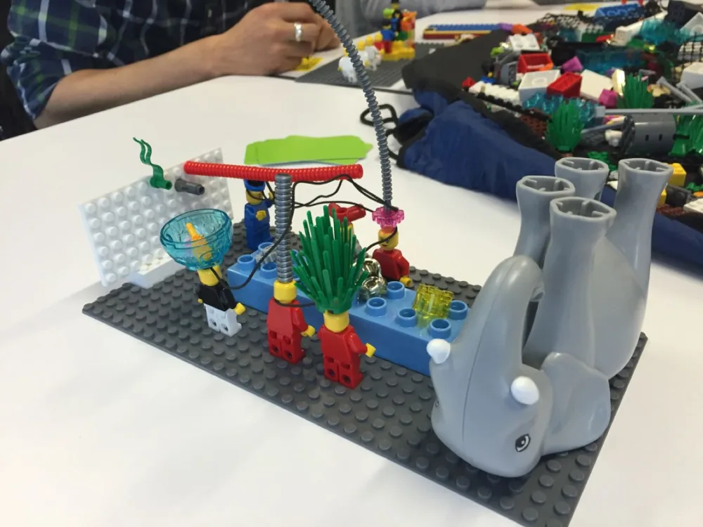 Hands assembling a LEGO Serious Play model featuring a dolphin during a Brick Spark workshop
